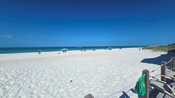 A beach with white sand, clear blue water, and a few umbrellas.