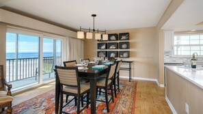 A dining area with a view of the ocean, a kitchen with a sink and wine bottle, and a decorative wall with framed items. - Coastal Luxury on the Gulf | Pool, Tennis & Trolley Beachfront Bliss on Anna Maria Island | Sleeps 6 (Holmes Beach)