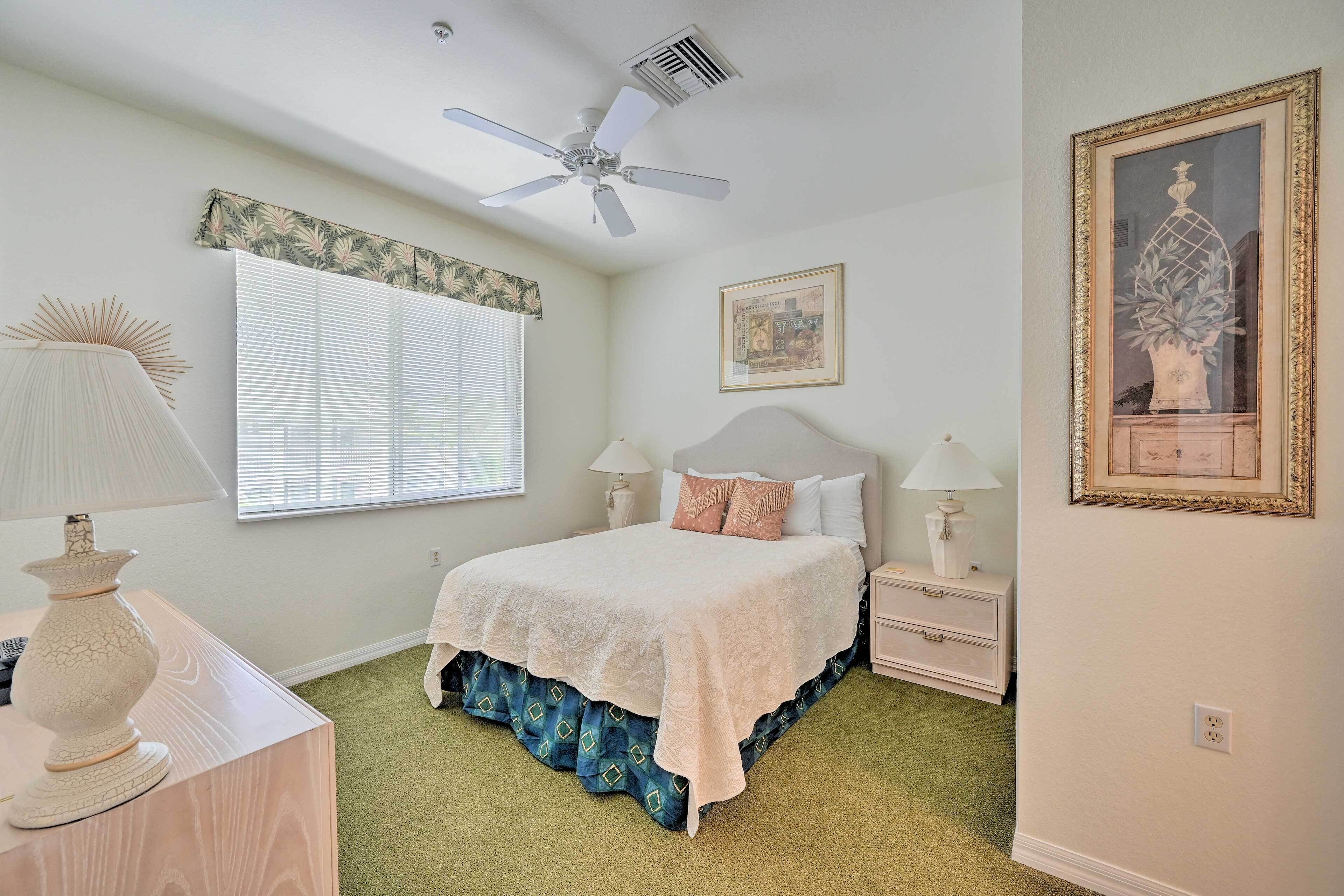 A bedroom with a bed, nightstands, a ceiling fan, a window with blinds, and a framed picture on the wall.
