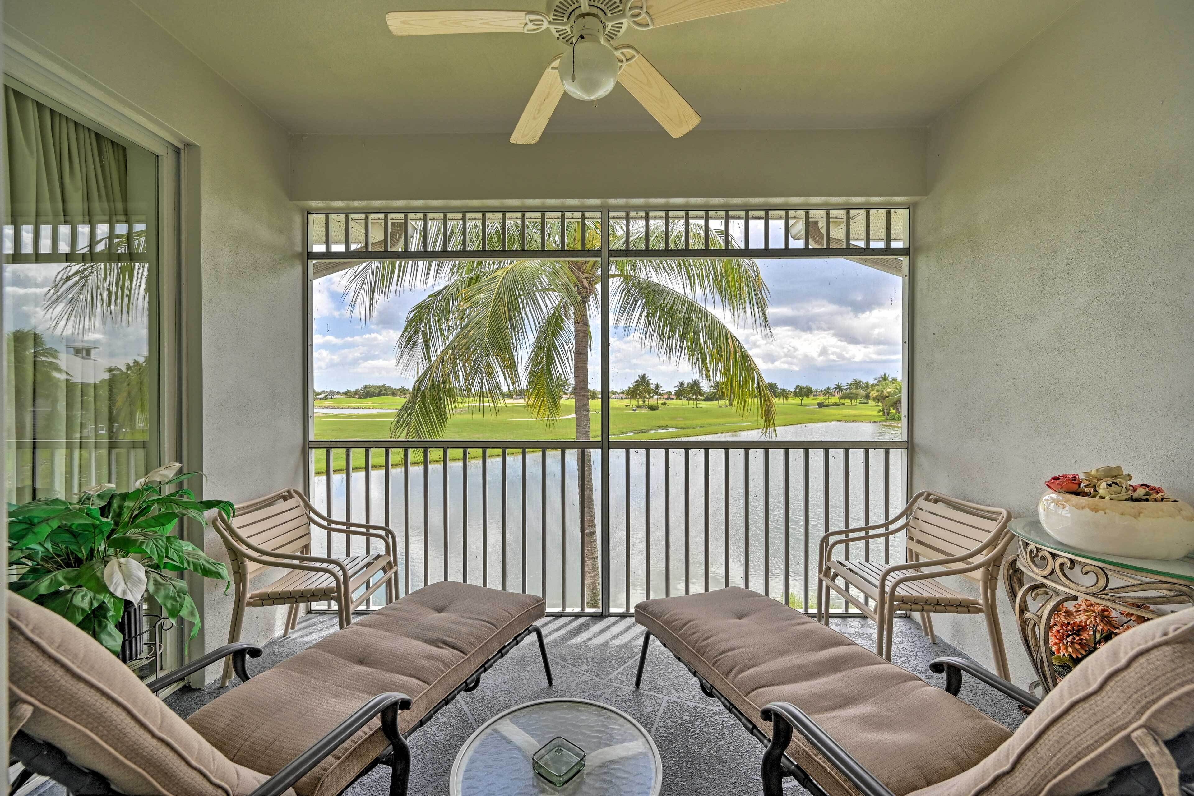 A balcony with two cushioned chairs, a glass table, and a ceiling fan.