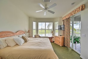Een slaapkamer met een bed, een plafondventilator, een televisie, een dressoir en een schuifdeur naar een balkon.