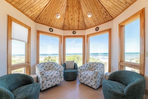 A room with a wooden ceiling, large windows, and two patterned chairs. - So Good - Corolla, Crown Point, Oceanfront, Ocean View, Pool, Hot Tub, Pool Table (Corolla)