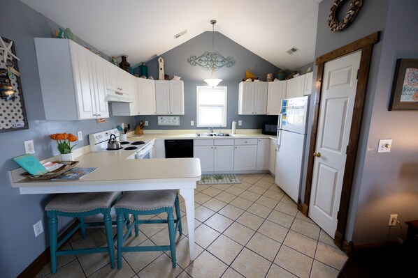A kitchen with white cabinets, a central island with bar stools, a chandelier, and a window.