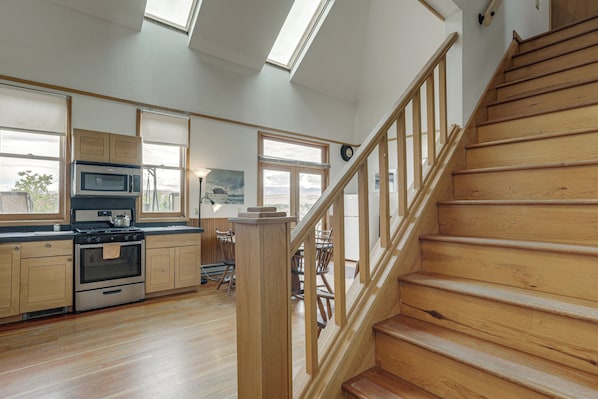 Cocina amplia con suelo de madera, una escalera de madera y ventanas grandes.