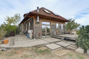 Een landelijke houten woning met een metalen dak, een terras en een groot raam.