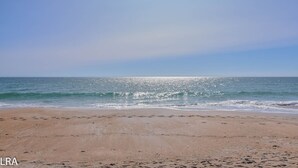 Une plage où l’on voit des empreintes de pas menant à l’eau, un ciel dégagé et des vagues calmes.