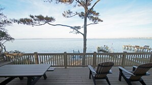 En træterrasse med picnicborde og Adirondack-stole med udsigt over et roligt vandareal.