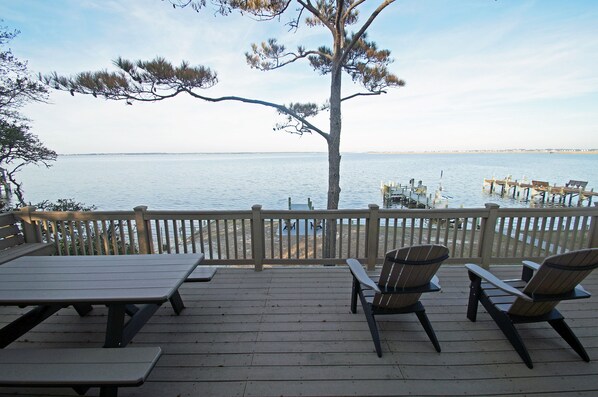 Une terrasse en bois, dotée de tables de pique-nique et de chaises Adirondack, surplombe un plan d’eau paisible.