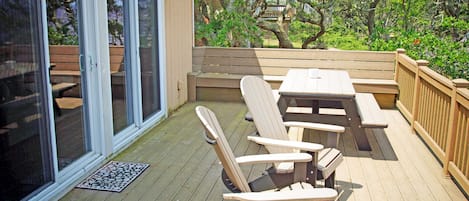 Una terraza de madera con una mesa, sillas, un ventanal corredero y una valla de madera.
