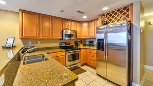 A modern kitchen with wooden cabinets, stainless steel appliances, granite countertops, and a built-in wine cooler. - Bright, welcoming 3-bedroom luxury condo with WiFi and an outdoor pool located uptown and just a block to the beach! (Ocean City)