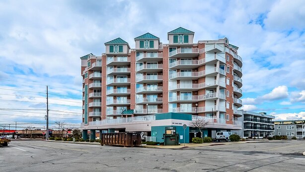 A multi-story hotel with balconies, a covered entrance, and a parking lot. - Bright, welcoming 3-bedroom luxury condo with WiFi and an outdoor pool located uptown and just a block to the beach! (Ocean City)