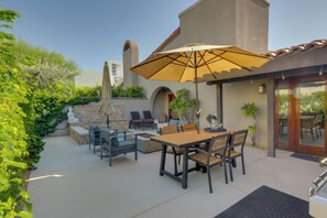 An outdoor patio with a table and chairs, a large umbrella, and a stone wall. - Dtwn Palm Springs Condo: BBQ, Pool, Fire Pit, etc! (Palm Springs)
