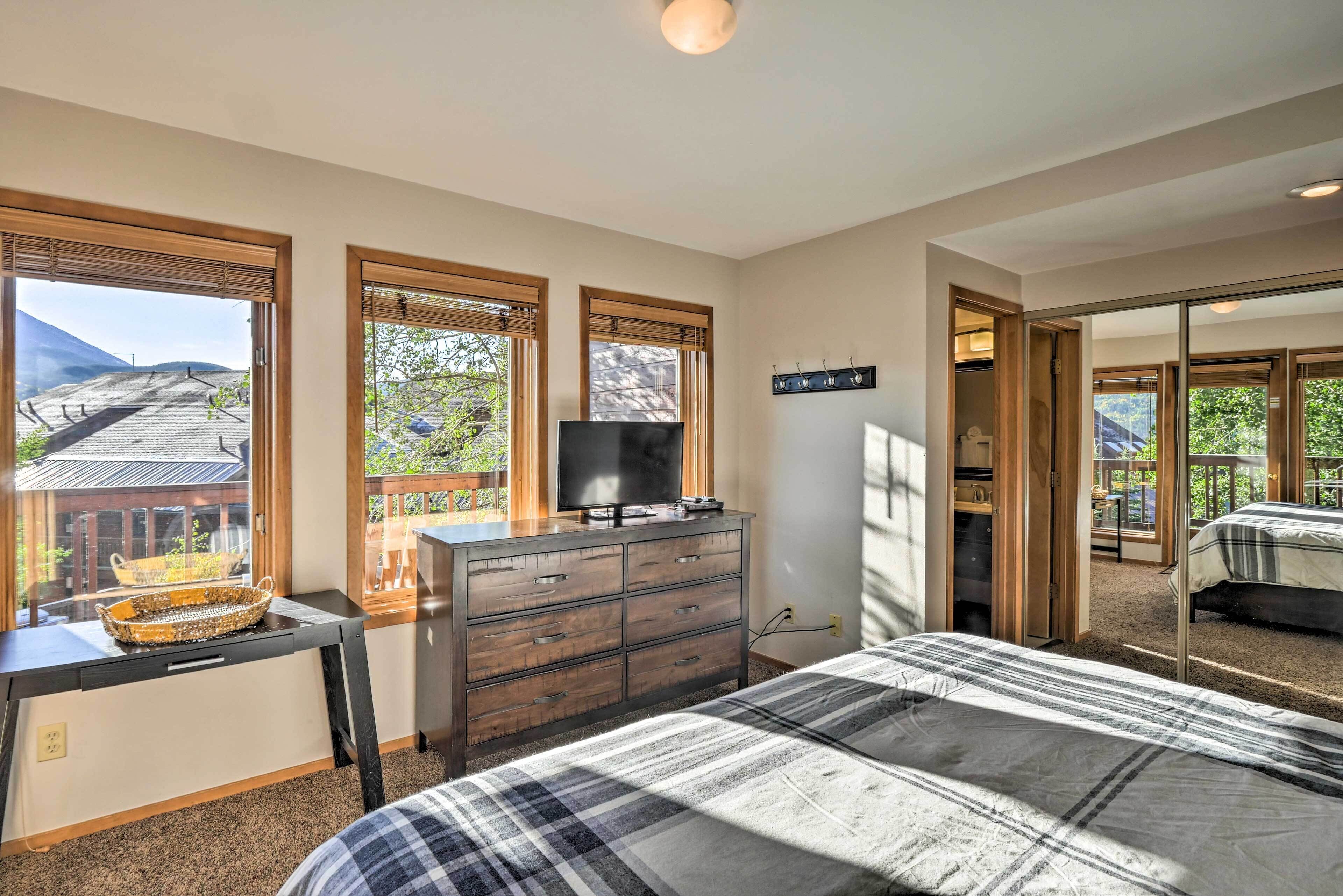 Un dormitorio con cama, cómoda, televisor y ventana con vista a la montaña y árboles.