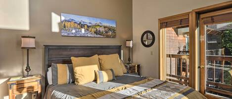 A bedroom with a bed, two bedside tables, a wall-mounted clock, and a large window with a view of the outdoors.