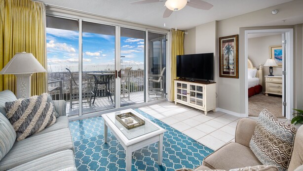 A spacious living area with a balcony, a flat-screen TV, and a dining table. - IP 202: Gulf Dwelling -  Welcome to Your Beachfront Paradise! (Fort Walton Beach)