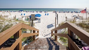 A wooden staircase leading to a beach with umbrellas and a sign. - IP 202: Gulf Dwelling -  Welcome to Your Beachfront Paradise! (Fort Walton Beach)