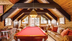 A cozy room with a pool table, wooden ceiling beams, a sofa, and a window with a view of trees. - Discount Available! Lake Tahoe Gem w/ Pool Table (South Lake Tahoe)