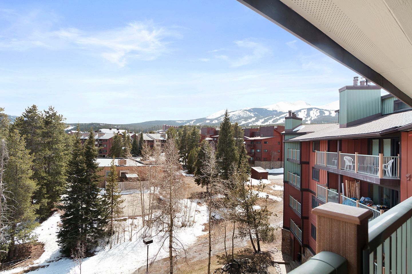 Une vue d’un immeuble à étages, doté de balcons, et d’un paysage enneigé avec des arbres et des montagnes en arrière-plan.