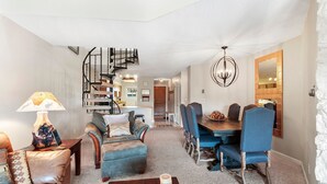 Un salón amplio con comedor, una escalera en espiral y una cocina al fondo.