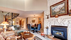 Una sala de estar acogedora con chimenea, un comedor y una escalera que sube a otro nivel.