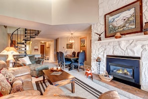 Cozy living room with a fireplace, comfortable seating, and dining area, featuring a spiral staircase and a beautiful painting.