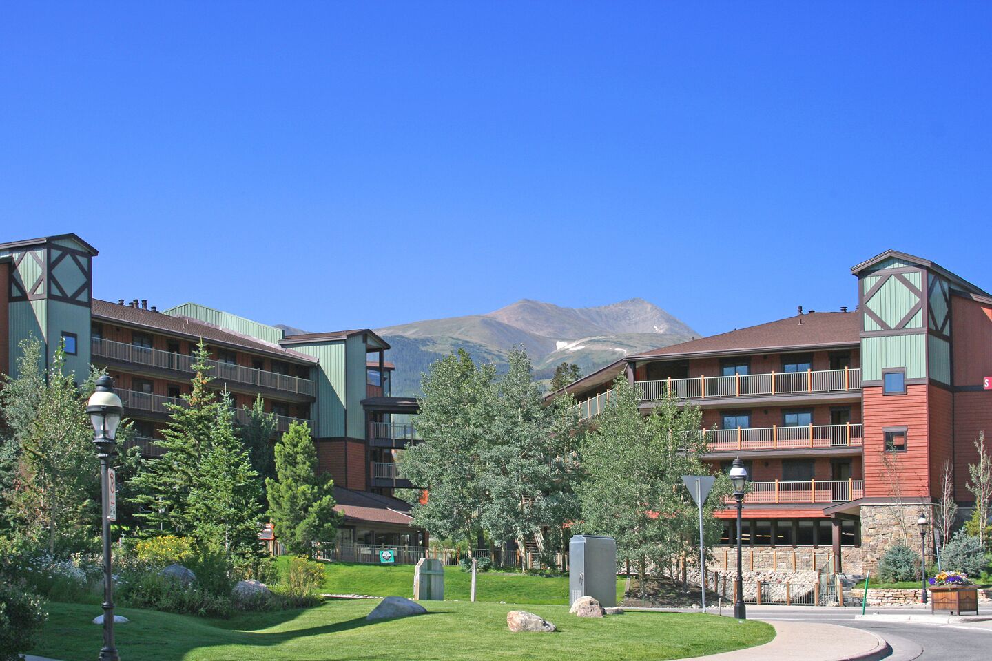 Un hotel con varios balcones, un césped bien cuidado y montañas al fondo.