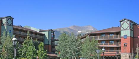 Un hotel con varios balcones, un césped bien cuidado y montañas al fondo.