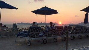 A beachside lounge area with sun loungers and umbrellas, overlooking the sea.