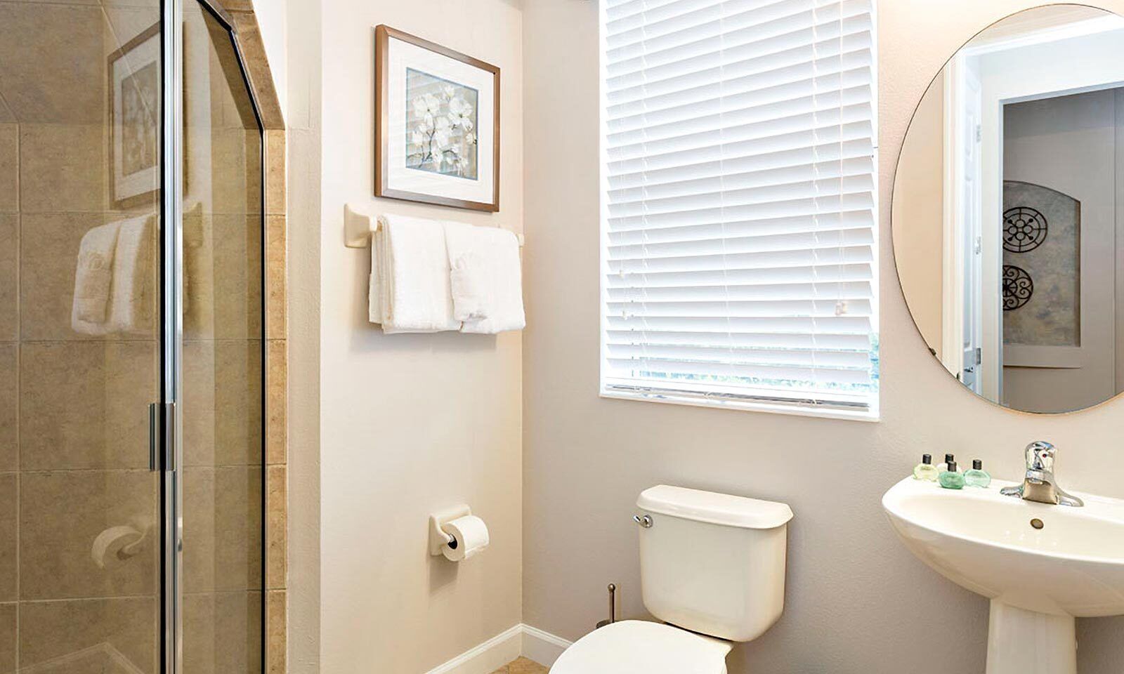 Ein Badezimmer mit Duschkabine aus Glas, Toilette, Waschbecken mit Pflegeprodukten und einem gerahmten Bild an der Wand.