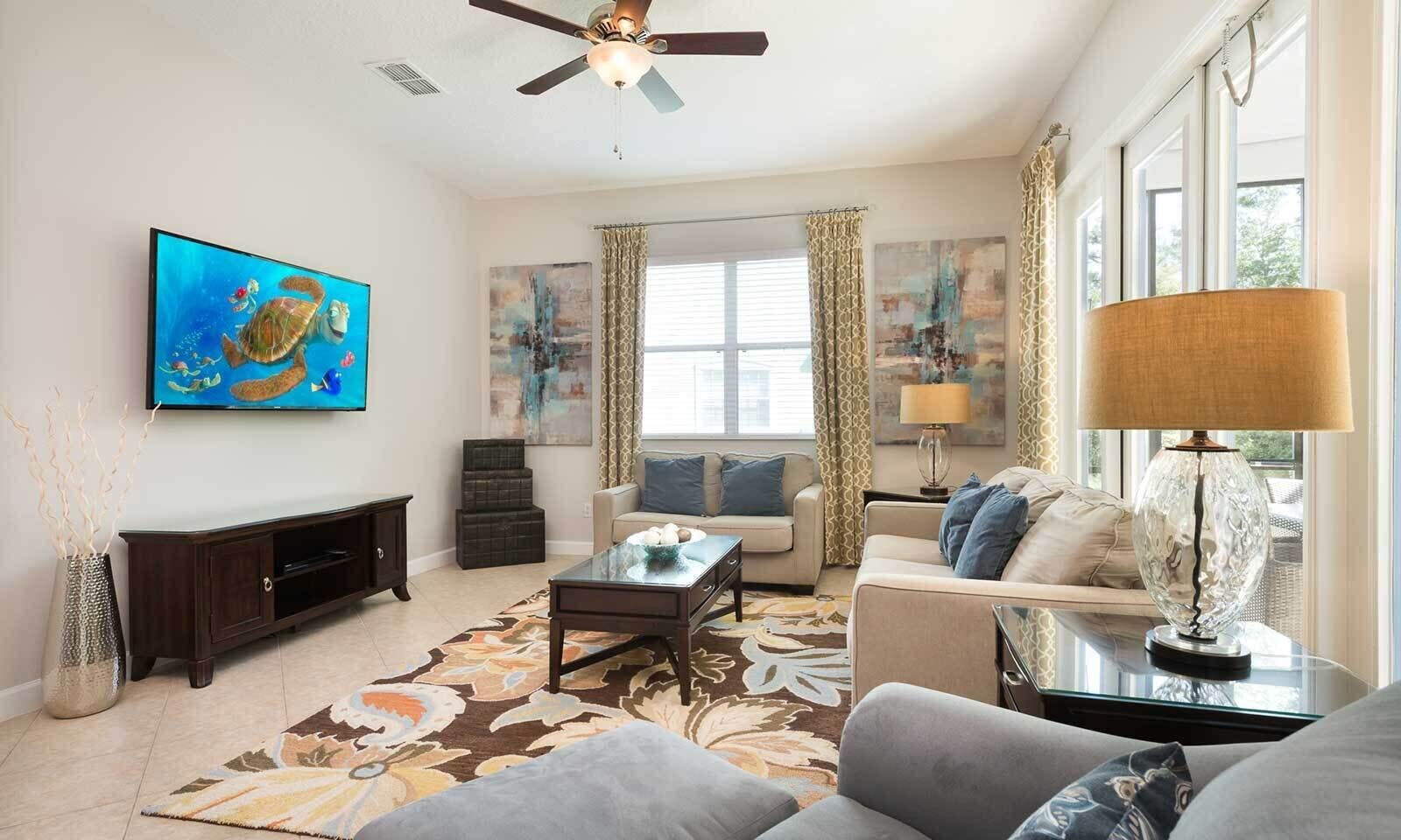 A living room with a ceiling fan, a flat-screen TV, a coffee table, sofas, and a patterned rug.