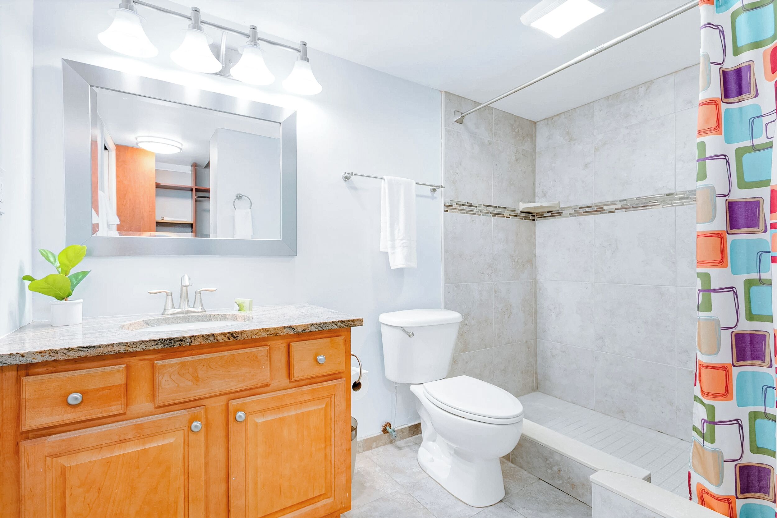 A modern bathroom with a wooden vanity, a large mirror, a toilet, and a shower area.