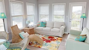 A sunlit living room with a white sofa, wicker chairs, and a colorful rug.