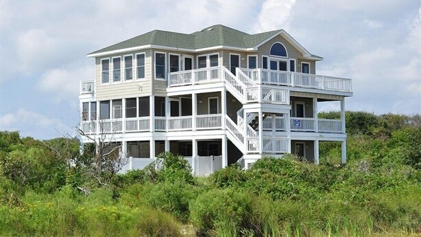 A large, multi-story house with balconies and a wrap-around porch, surrounded by greenery.