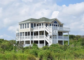 A large, multi-story house with balconies and a wrap-around porch, surrounded by greenery.