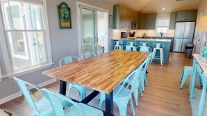 A dining area with a wooden table and light blue chairs, a kitchen with green cabinets, and a view of the outside through a sliding door.