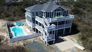 A two-story beach house with a swimming pool, multiple balconies, and a covered deck area.