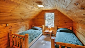 Une cabane chaleureuse avec deux lits en bois, une petite table et une fenêtre donnant sur la forêt.