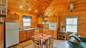 L’intérieur d’une cabane avec des murs en bois, un coin repas comprenant une table et des chaises, une cuisine équipée et une tête d’animal empaillée accrochée au mur.