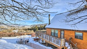 Une cabane en bois dotée d’une terrasse, entourée d’un paysage enneigé et avec des montagnes en arrière-plan.