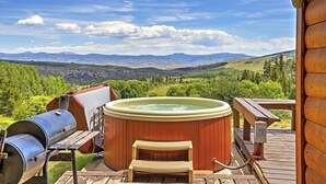 Un bain à remous sur une terrasse en bois, avec vue sur les montagnes et la verdure.