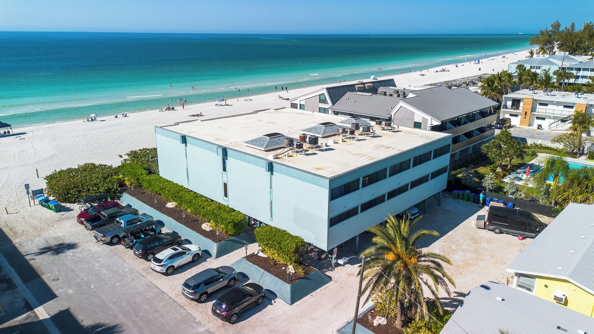 A modern building with a flat roof, parking lot, and a view of the beach and ocean.