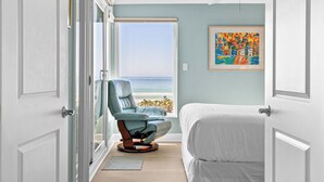 Une chambre avec vue sur la plage, une chaise, un lit et un ventilateur de plafond.
