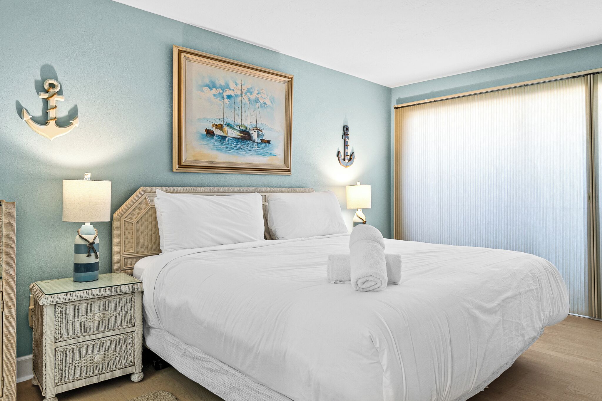 Habitación de hotel con una cama grande, dos lámparas de noche, un cuadro de un velero y un ancla decorativa en la pared.