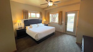 A hotel room with a bed, two bedside lamps, a ceiling fan, a window with curtains, and a door with a view of the outside. - Two Bedroom Condo @ Spring Brook Resort (Wisconsin Dells)