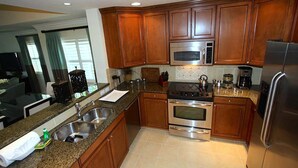 A kitchen with wooden cabinets, stainless steel appliances, granite countertops, and a double sink. - Sun Kissed Condo with Balcony Access at Reunion (Kissimmee)