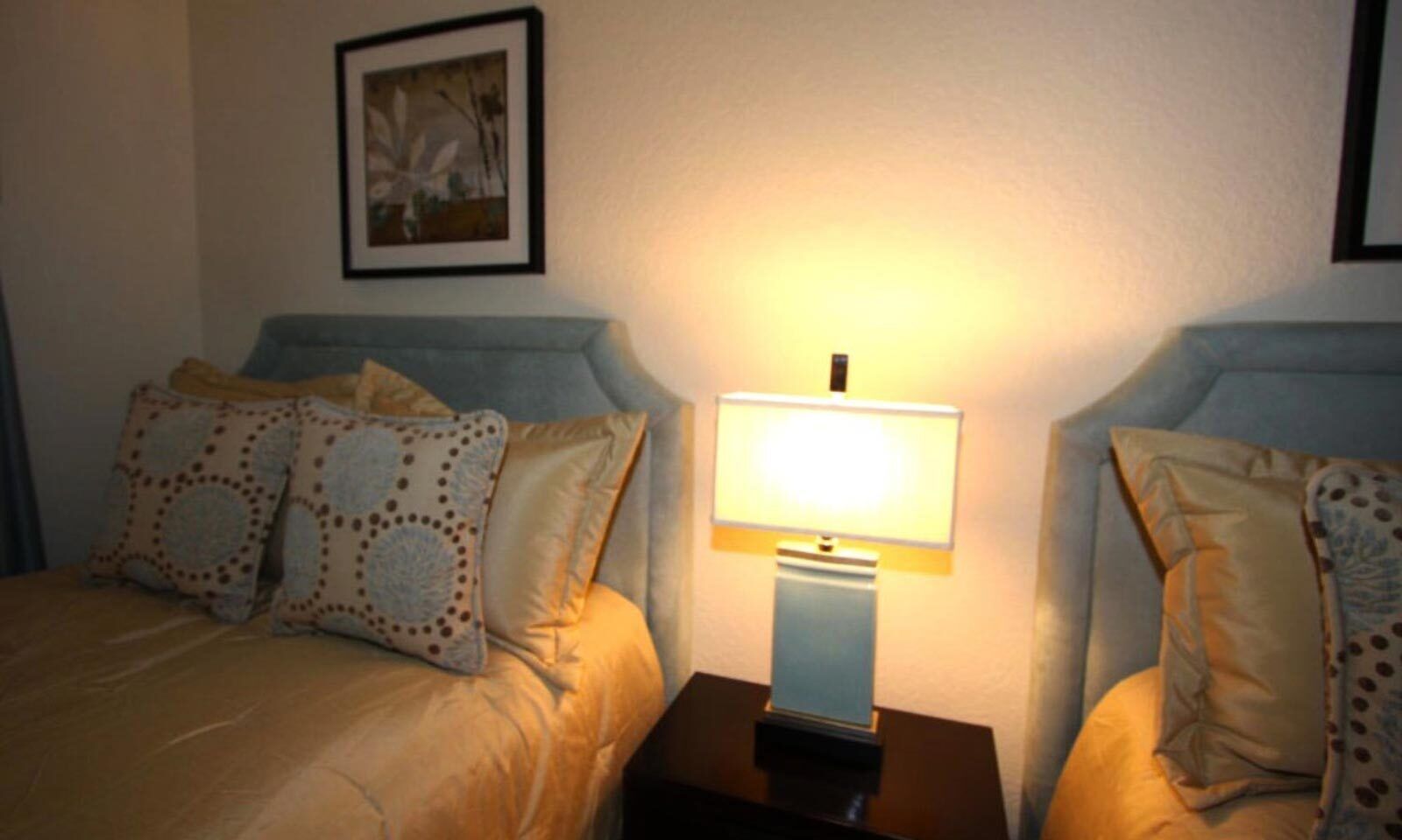 A bedroom with two beds, a nightstand with a lamp, and a framed picture on the wall.