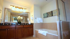 A bathroom with a wooden vanity, a large mirror, a bathtub, and a glass shower enclosure. - Sun Kissed Condo with Balcony Access at Reunion (Kissimmee)