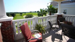 A balcony with a view of a golf course, a brick column, and outdoor furniture. - Sun Kissed Condo with Balcony Access at Reunion (Kissimmee)