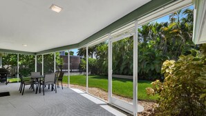 Um alpendre coberto com mesa e cadeiras, grandes portas de vidro e vista para um jardim bem cuidado.