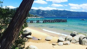 Ein Strand mit einer Holzsteganlage, die sich ins Wasser erstreckt, umgeben von großen Felsen und einer bergigen Kulisse.